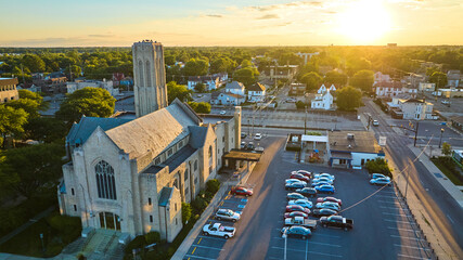Glorious golden sun behind church at sunset aerial, Muncie IN with neighborhood of houses