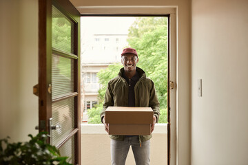 Smiling African delivery man standing at a front door carrying packages