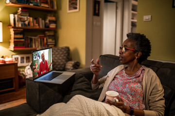 Senior African American woman consulting her therapist via a video call on the laptop on the couch at home