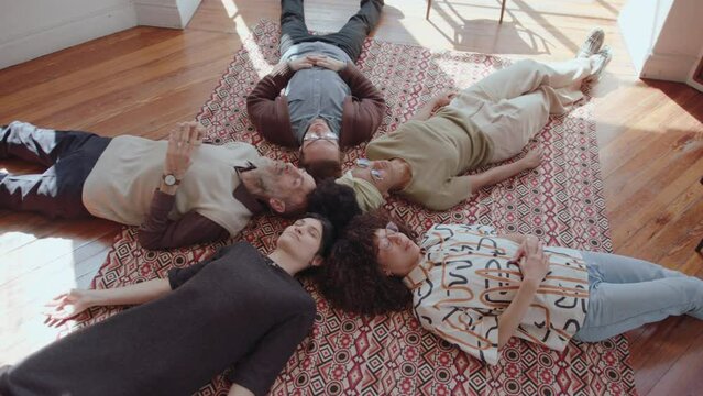 Group of people lying down on the floor with eyes closed and telling the truth while participating in a therapy session during support group meeting. High angle view