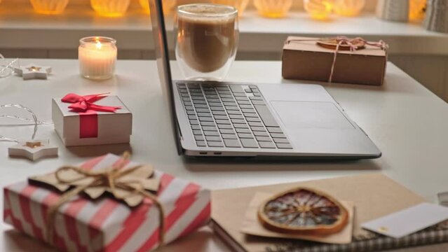 Notepad with a pen, laptop, coffee cup, wrapped gifts on a desk table. Winter Festive atmospheric mood. Preparation for Christmas. Business Holidays Concept. Freelancer's desktop during Xmas vacation