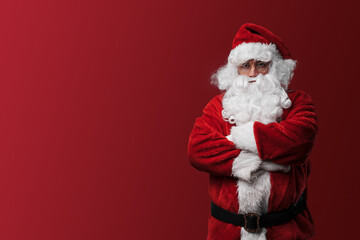 Serious Santa Claus in red costume posing with crossed arms against a red background