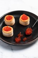 Tartlets with red caviar on a black plate
