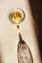 One glass of cognac sparkling at sunlight, beige background with dark shadow and reflection, sun...