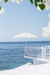 Fototapeta premium A large white umbrella on the background of the blue ocean. Stylish concept of beach holidays and resorts. Beautiful view from the hotel while traveling