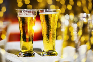 A glass of beer on table with blur light gold bokeh at relax moment in restaurant.