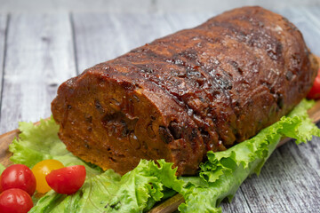 Vegan meat- seitan- ham shaped and served on wooden tray, salad greens. Wooden table, copy space