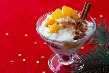 Christmas dessert, gingerbread with orange, whipped cream and cinnamon in cup on red background