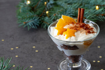 Christmas dessert, gingerbread with orange, whipped cream and cinnamon in cup on dark background
