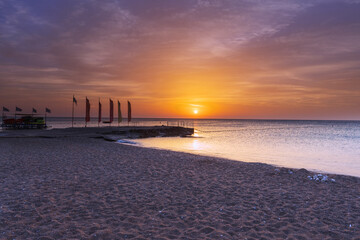 Rhodes island pebble beach, pier with flags and beautiful sunrise with dramatic sky with clouds.