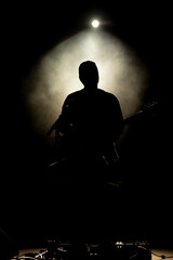 Musician playing guitar performing on stage under spot light. Silhouette of a music artist and band...