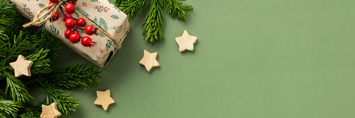 Christmas festive banner, fir branches and gift boxes with a sprig of rowan and wooden stars on a green background, top view