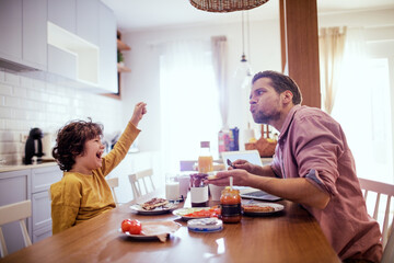 Happy father eating breakfast with little son in the kitchen at home