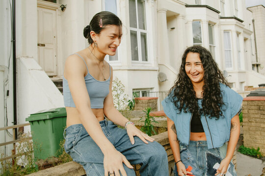 Two multiracial non-binary friends in fashionable outfits hanging out outdoors having fun
