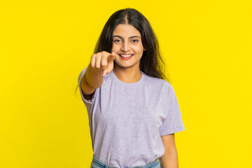 I choose you. Indian smiling woman pointing finger to camera and looking with playful happy expression, making winner choice, showing direction. Arabian young girl isolated on yellow studio background - obrazy, fototapety, plakaty