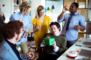 Businessman holding gift celebrating birthday with colleagues in office - obrazy, fototapety, plakaty
