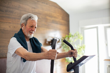 Senior man exercising on a fitness bike in the bedroom at home