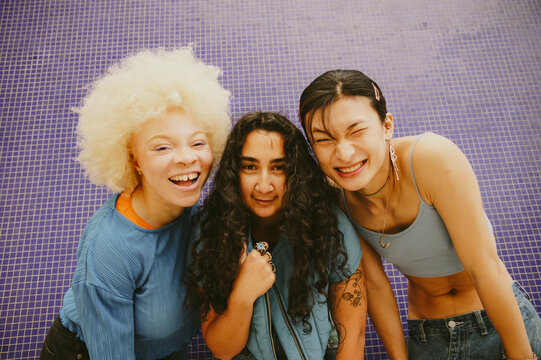 Vintage style portrait of three multiracial friends next to each other in front of blue wall laughing into camera