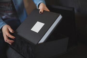 Female hands holding a beautiful leather black bound book in box with soft fabric. Wedding photo book,family album. The texture of the cover of a photobook made of genuine leather. Photobooks for gift