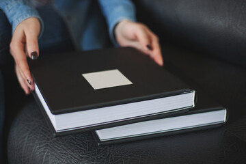 Female hands holding a beautiful leather black bound book in box with soft fabric. Wedding photo...