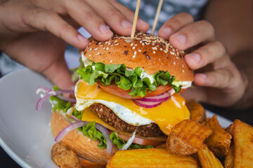 Hands holding a crispy veggie burger with egg, lettuce, cheese, tomato and onion. Served with french fries. Delicious american food. Vegetarian food. Fast food. 