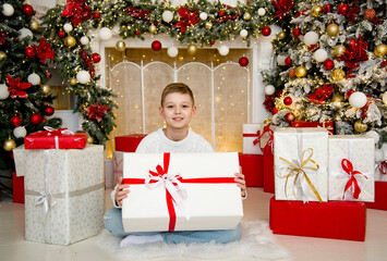 Obraz na płótnie Canvas little handsome smiling blonde boy sitting in beautiful decorated room and holding christmas gift