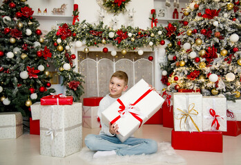 Obraz na płótnie Canvas little handsome smiling blonde boy sitting in beautiful decorated room and holding christmas gift
