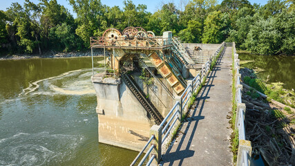 Bridge path Maumee River Dam rusting gears and equipment over water choked by trees and swirling...