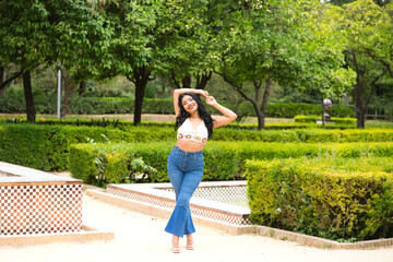 Fototapeta premium Young and beautiful Latin woman from South America walks among the trees and vegetation of the park. The woman is smiling and happy and is posing for photos. Travel and holiday concept.
