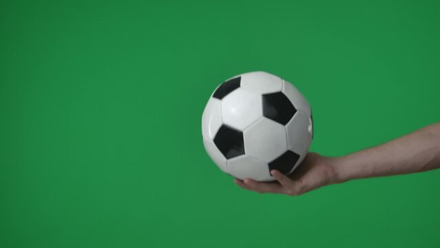 In a close up shot on a green background. a womans hand holds a soccer ball in the palm of her hand, it is inflatable and round. She points it toward the camera and is about to toss it