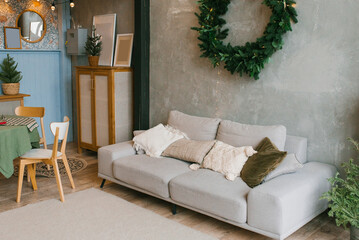 Rustic home interior of the living room with a Christmas wreath, sofa and Christmas tree. Decorations for the celebration of Christmas holidays
