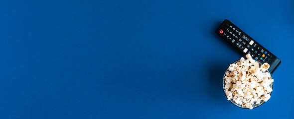 Popcorn and decorative pumpkins with TV remote on a blue background with copy space. Movie night concept. Wateching TV themed photo. Fall or autumn TV shows.