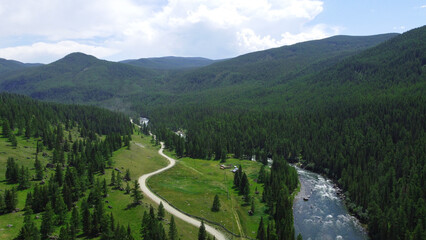 Aerial view of a green mountain landscape and alpine meadows where a river flows from the mountains and a beautiful coniferous forest stretches.