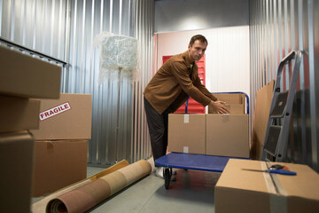 Mature man sorting boxes in storage unit he rents - Powered by Adobe