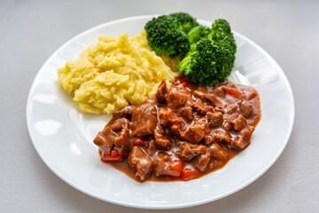 Beef stew on a plate with boiled potatoes and green broccoli