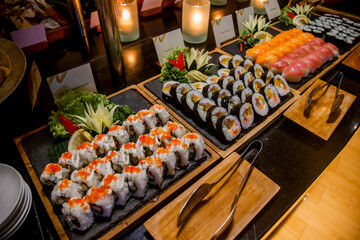 Sushi bar among catering banquet table. Variety of snacks, appetizers, seafood and cooked meals...