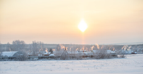 Frosty sunny day. Smoke comes out of the pipes above the village houses during heating. Rural winter landscape