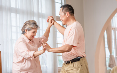 Asian sweet senior elderly couple wearing casual clothes, staying in indoor cozy home at living room, dancing together with happiness and passion, smiling. Retirement, Lifestyle, Healthcare Concept.