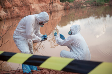 Two men wore PPE suits. One of them sat down and held up a glass bottle containing contaminated...