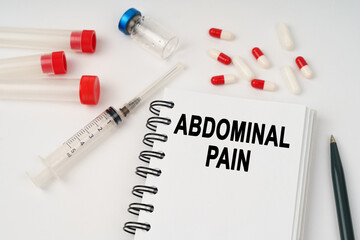 On the table are pills, injections, a syringe and a notepad with the inscription - Abdominal pain