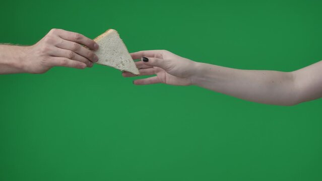 In the shot close up on the green background. The womans hand holds two pieces of bread with a triangular shape. She reaches out to the man, who takes a pastry with a dark and light piece