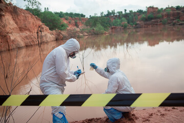 Two men wore PPE suits. One of them sat down and held up a glass bottle containing contaminated water to inspect it.