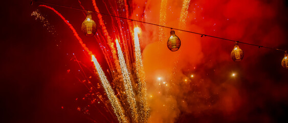 Bright red and orange fireworks against dark sky with lanterns during Chinese lunar new year celebration - 681668040
