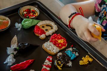 Close up of child's hand decorating Christmas gingerbread homemade cookies with colorful glaze.