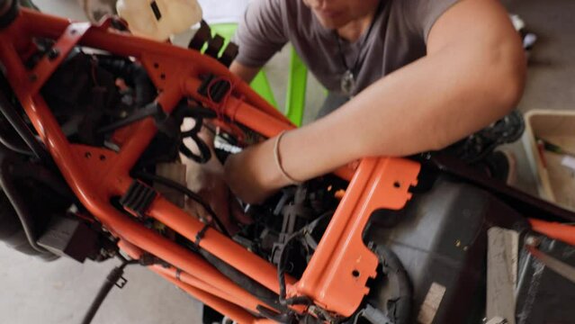 Asian Woman, 50, Expertly Repairing the Engine of an Orange Motorcycle