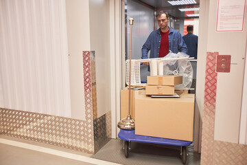 Man pushing cart with furniture and boxes when walking out of elevator in self-facility unit © AnnaStills