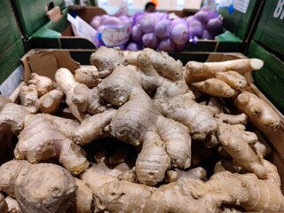 pieces of ginger lie in a cardboard box on a shelf in the vegetable department of a supermarket