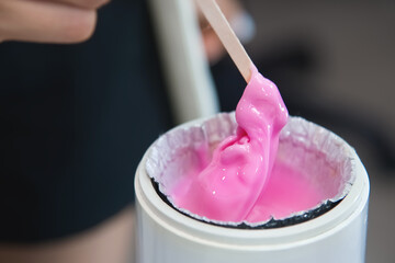 Wax in heating container. The cosmetologist uses hot wax for depilation and prepares it in a special device. Preparation of pink wax for sugaring.