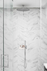 A luxury shower detail with marble herringbone tiles, polished chrome showerhead, and a glass door.