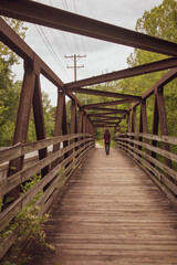 Fototapeta na wymiar Walking into the future - a person walking away from the camera across a boardwalk footbridge in a nature area